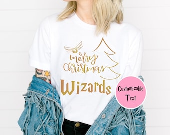 May include: White t-shirt with a gold-colored design featuring a Christmas tree, a flying object, and the words "merry Christmas Wizards." A pink circle with the words "Customizable Text" is on the right.