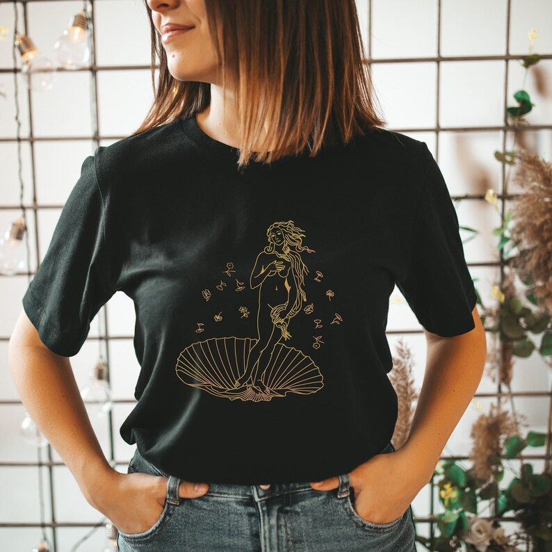 May include: Black t-shirt with a gold outline illustration of the Birth of Venus, a famous Renaissance painting by Sandro Botticelli.