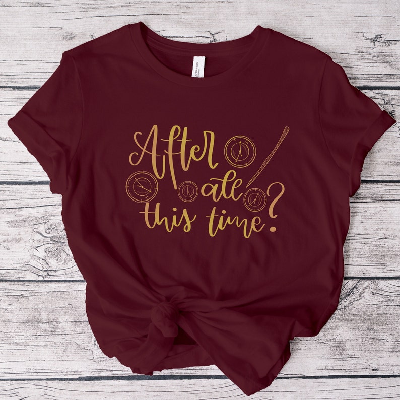 A picture showing a layed out Bella Canvas Unisex 3001 t-shirt in maroon color with the words after all this time; in cursive gold lettering and with wizard symbols.
