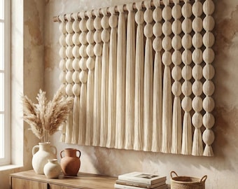 May include: A wall hanging made of cream-colored yarn, featuring vertical rows of spherical knots and long, straight fringe suspended from a horizontal wooden rod. The piece displays a textured, layered design with varying lengths of fiber strands.