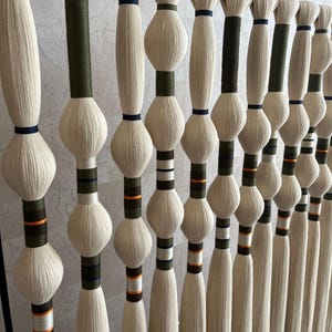 May include: A wall hanging made of white yarn with green, orange, and blue stripes. The yarn is tied together in a series of knots, creating a textured and visually appealing design.