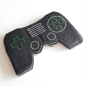 Könnte beinhalten: Schwarze und grüne Servietten in Form eines Gamepads. Das Gamepad hat einen weißen Umriss und ein grünes Pluszeichen.