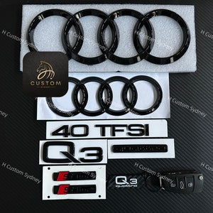 May include: A set of black Audi car emblems, including a set of four rings, a 40 TFSI emblem, a Q3 emblem, and a Q3 quattro emblem. The emblems are on a white background.