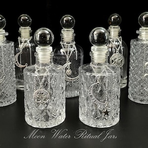 May include: An array of clear glass jars with decorative stoppers and silver charms. The jars have various shapes and are adorned with charms including moons, stars, and snakes. The text "Moon Water Ritual Jars" is at the bottom.