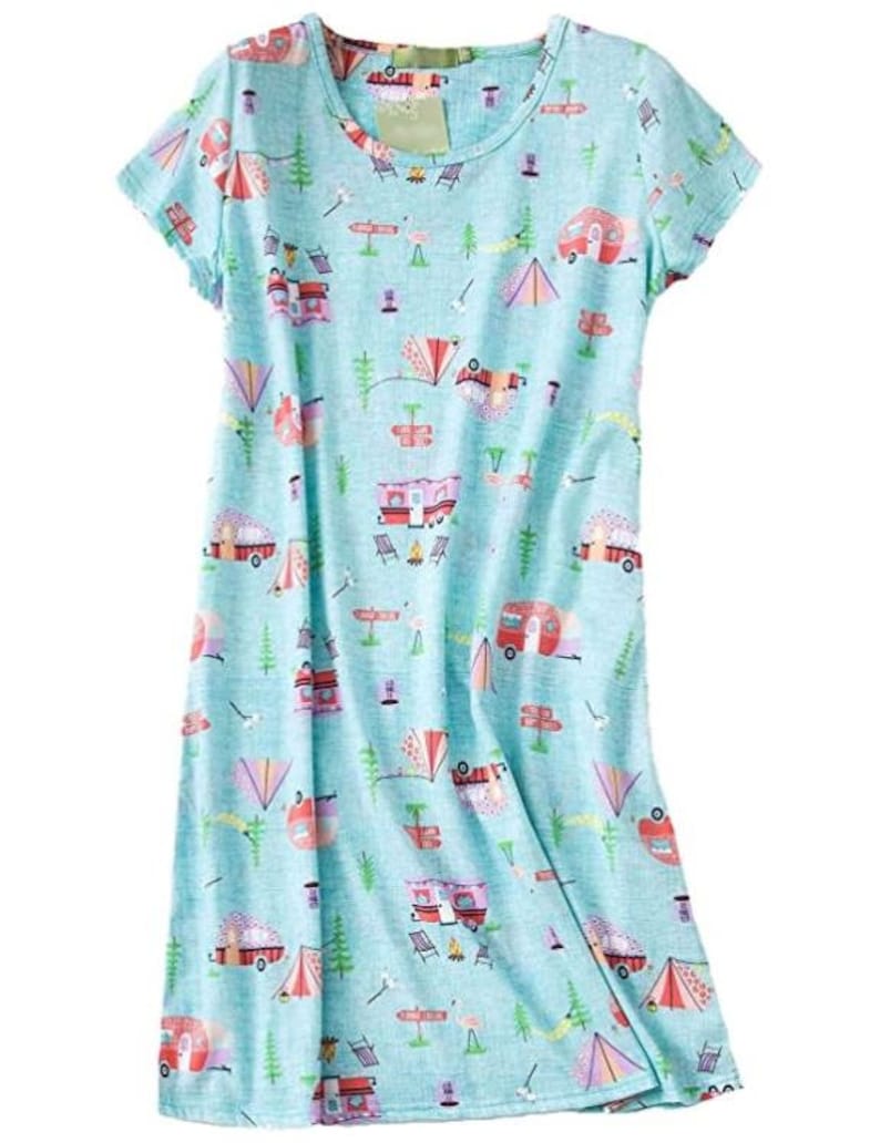May include: A light blue, short-sleeved dress with a camping-themed pattern. The print includes red and pink camper vans, tents, trees, and camping chairs. The dress has a round neckline and a relaxed fit.