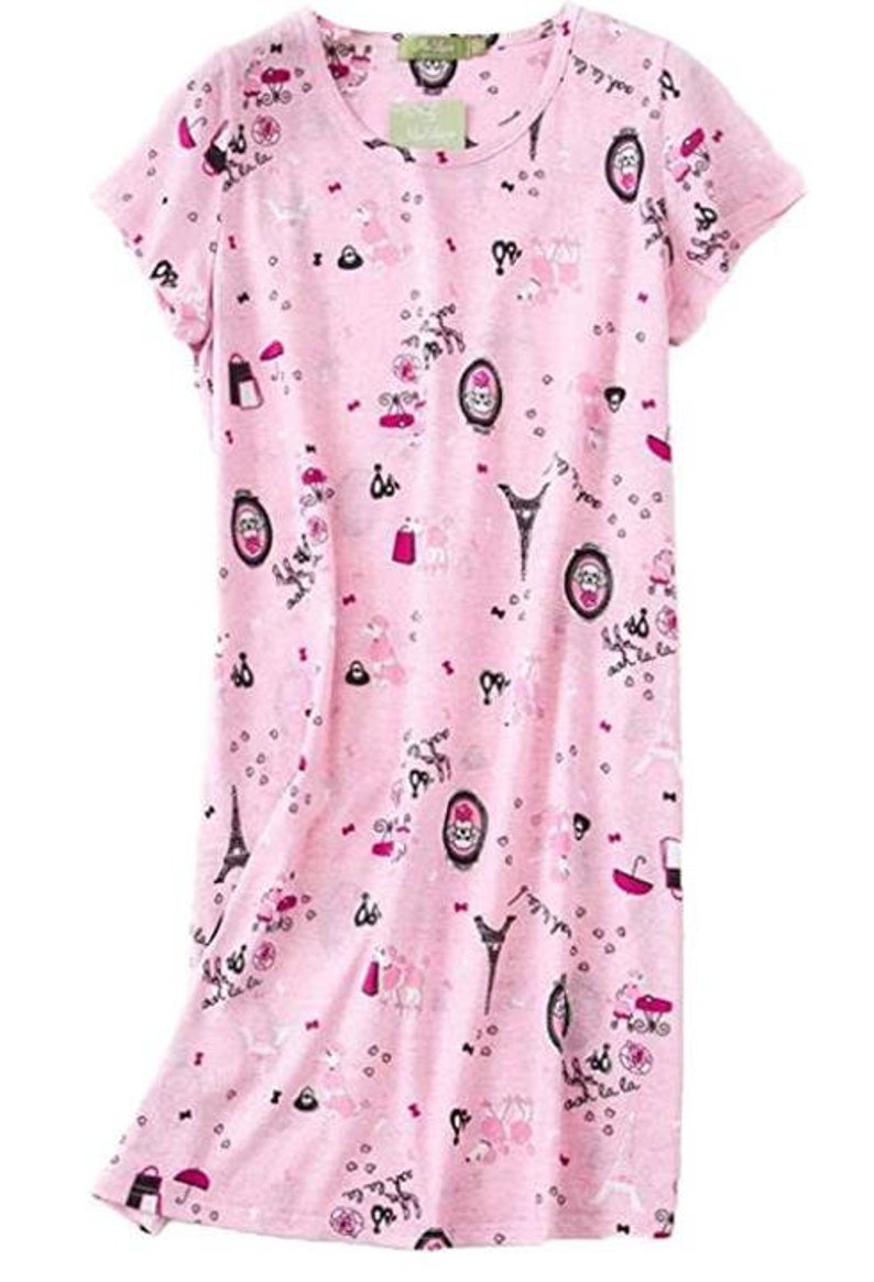 May include: A pink short-sleeved nightgown with a round neckline. The fabric is covered in a repeating pattern of Parisian-themed illustrations, including the Eiffel Tower, umbrellas, and portraits. The nightgown has a relaxed fit.