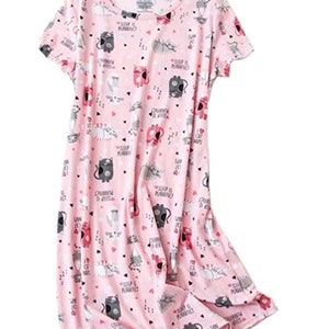 May include: A pink short-sleeved nightgown with a pattern of cartoon cats, hearts, and the phrase "Sleep is Purrfect". The cats are in various poses and colors, including gray, black, and red. The nightgown is made of a soft fabric.