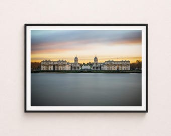 May include: A framed photograph of a waterfront scene featuring large, symmetrical buildings with columns and domes. The buildings are reflected in the calm water, under a colorful sunset sky. The photograph is in a black frame.