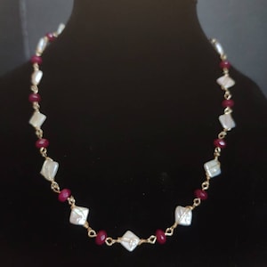 May include: A gold necklace with white and red beads. The necklace is made with wire wrapped beads and features a delicate design.