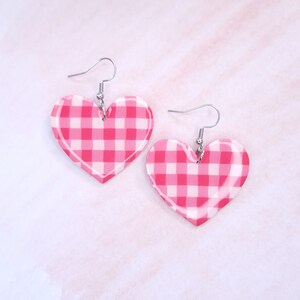 May include: A pair of pink and white gingham heart-shaped earrings with silver hooks.