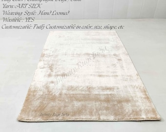 Puede incluir: Una alfombra rectangular tejida a mano en tonos beige champán y arena. El texto en la imagen dice: Rug Color: Champagne Beige/Sand, Yarn: ART SILK, Weaving Style: Hand Loomed, Washable: YES, Customizable: Fully Customizable, Infinity Rugs India.