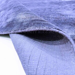 May include: Close-up of a blue and gray rug with a textured surface. The rug is folded over, revealing the underside, which is a lighter shade of blue.