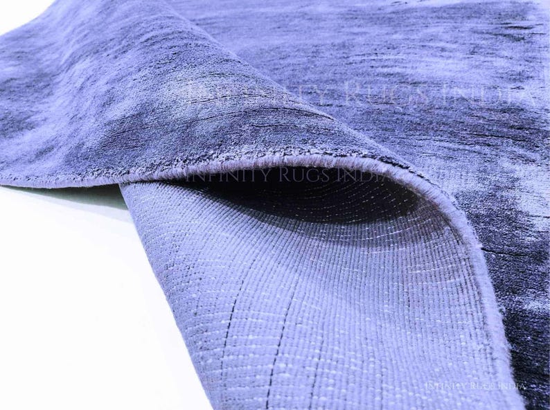 May include: Close-up of a blue and gray rug with a textured surface. The rug is folded over, revealing the underside, which is a lighter shade of blue.