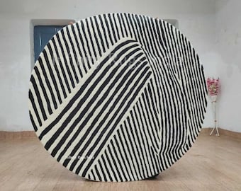 May include: A large, round, black and white striped rug with a geometric pattern. The rug is made of wool and has a soft, plush texture.
