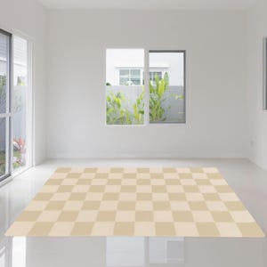 Pode incluir: Um tapete xadrez bege e creme numa sala clara com paredes brancas. O tapete é retangular e cobre uma grande parte do chão. Uma janela com vegetação é visível no fundo.