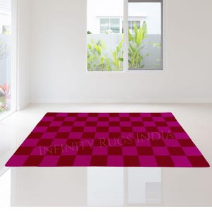 Pode incluir: Um tapete xadrez rosa e bordô com o texto "INFINITY RUGS INDIA" no centro.