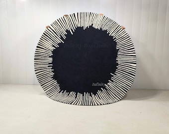 May include: A round rug with a dark navy center and a white, linear pattern radiating outwards. The design creates a sunburst effect. The rug is placed on a white surface. The text "Infinity Rugs India" is visible.