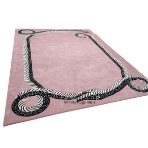 Może przedstawiać: R&oacute;żowy dywan z czarno-białym wzorem węża wok&oacute;ł krawędzi. Dywan ma nadrukowany tekst "Infinity Rugs India".