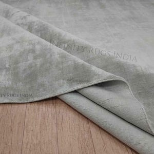 Puede incluir: Primer plano de una alfombra gris claro con un sutil patr&oacute;n de m&aacute;rmol. La alfombra est&aacute; doblada por la mitad, revelando la parte inferior, que es de un tono gris m&aacute;s claro.