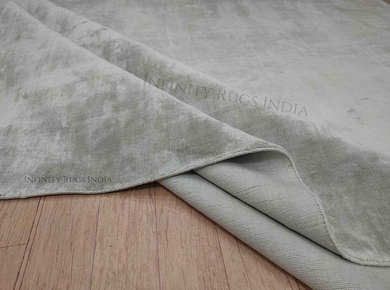 Puede incluir: Primer plano de una alfombra gris claro con un sutil patr&oacute;n de m&aacute;rmol. La alfombra est&aacute; doblada por la mitad, revelando la parte inferior, que es de un tono gris m&aacute;s claro.