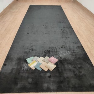 Puede incluir: Una alfombra negra con un aspecto sutilmente desgastado. La alfombra está colocada sobre un suelo de madera y tiene algunas pequeñas muestras de tela colocadas sobre ella.