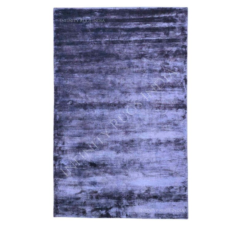 May include: A blue and gray abstract patterned rug with a subtle sheen. The rug has a contemporary design and is made of high-quality materials. "Infinity Rugs India" is printed in the bottom right corner of the rug.