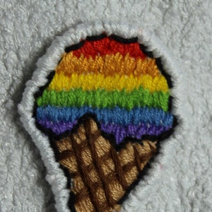 Könnte beinhalten: Ein gestickter Patch in Form eines regenbogenfarbenen Eisbechers mit einem braunen Waffelkegel. Der Patch ist aus buntem Garn gefertigt und hat einen schwarzen Umriss.