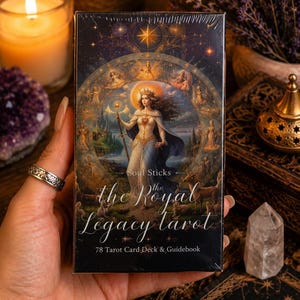 May include: A rectangular tarot card deck box titled The Royal Legacy Tarot by Soul Sticks. The front features a central illustration of a crowned figure holding a staff, surrounded by a circular frame of smaller figures, with 78 Tarot Card Deck & Guidebook text.