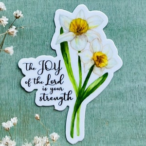 May include: A sticker featuring a watercolor illustration of two white daffodils with yellow centers and green stems. The sticker has the text "The JOY of the Lord is your strength" in black script. The background is a textured teal color.