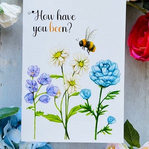 May include: A white card with the text "How have you been?" in black cursive font. A bee with black and yellow stripes is flying above a bouquet of white daisies, blue flowers, and green leaves.