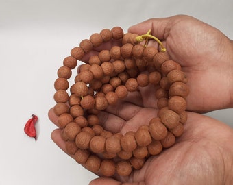 May include: A brown mala bead necklace with a yellow string. The necklace is made of round beads and is held in a person's hands.