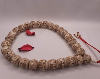 May include: A white bone bead necklace with a red string tassel. The beads are carved with skull designs.