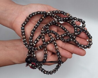 May include: A long strand of brown and white beads with a black tassel. The beads are round and have a white pattern on them.