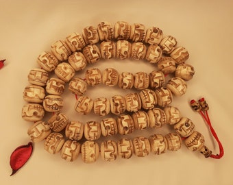 May include: A white bone mala with a skull design on each bead. The mala has a red string tassel.