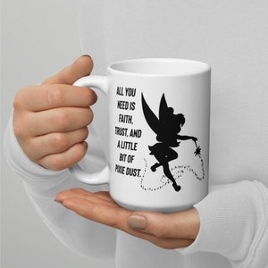 Puede incluir: Taza de cerámica blanca con una silueta negra de Campanilla y la cita "Todo lo que necesitas es fe, confianza y un poco de polvo de hada."