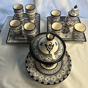 Puede incluir: Un juego de tazas de té y tetera marroquíes en blanco y negro con intrincados patrones geométricos. El juego incluye una tetera, seis tazas de té y dos platillos. Las tazas de té y la tetera están hechas de cerámica y tienen un acabado brillante.