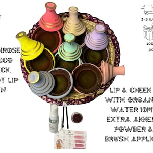 Puede incluir: Un conjunto de siete ollas de barro marroquíes de colores con detalles dorados, dispuestas en una cesta tejida. Las ollas están llenas de una sustancia marrón oscura. El conjunto incluye una pequeña botella de líquido, un pequeño recipiente de polvo y dos aplicadores de brocha para labios.  Lip & Cheek Stain with Organic Rose Water 10ml, Free Extra Akker Fassi Powder & 2 Lip Brush Applicators.