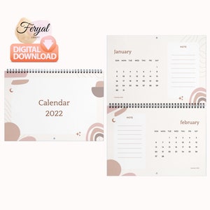 Op de afbeelding: Een spiraalgebonden kalender voor 2022 met een minimalistisch ontwerp. De omslag leest "Kalender 2022" met abstracte vormen in beige en bruin. De open kalender toont januari en februari, met ruimte voor notities. "Digitale download" is zichtbaar.