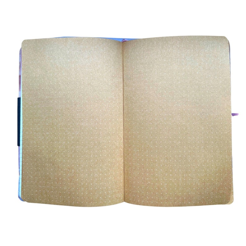 May include: Open notebook with dot grid pages. The pages are a light brown color with small white dots. The notebook is open to reveal two blank pages. The binding is black and the edges of the pages are a light purple color.