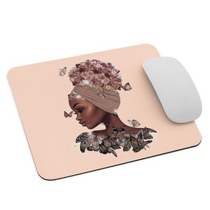 Op de afbeelding: Perzikroze muismat met een illustratie van een vrouw met een hoofddoek en bloemenkapsel. Vlinders omringen haar. Een witte draadloze muis bevindt zich rechts.