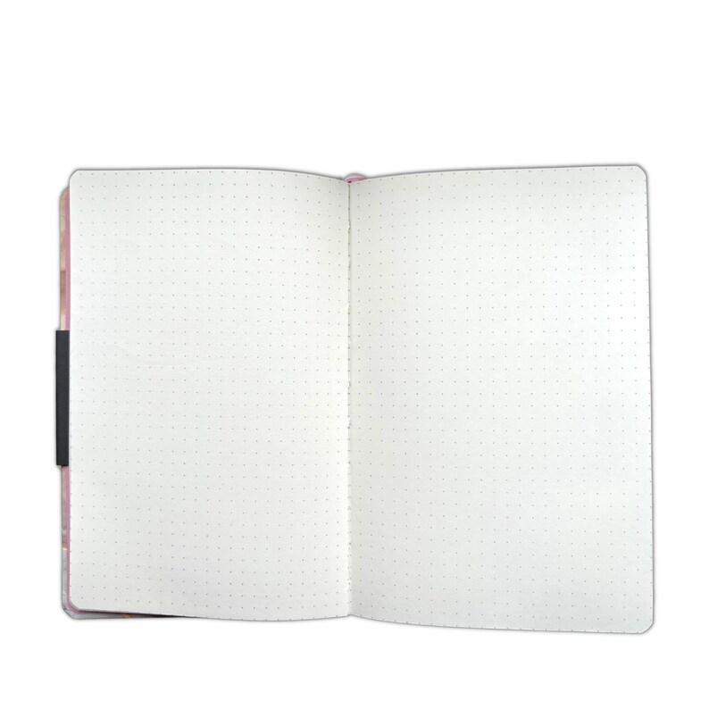 May include: Open, dot grid notebook with a pink floral cover and a black elastic closure. The pages are white with evenly spaced gray dots, perfect for journaling, sketching, or note-taking. The notebook is open, displaying the blank pages.