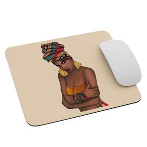 Op de afbeelding: Een beige muismat met een illustratie van een vrouw met een kleurrijke hoofddoek, gouden oorbellen en een oranje top. Haar armen zijn gekruist. Een witte draadloze muis bevindt zich rechts van de muismat.