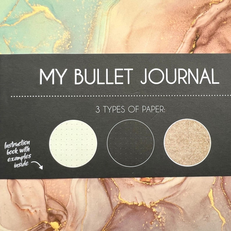 May include: A black journal cover with the words "MY BULLET JOURNAL" in white. Below, it reads "3 TYPES OF PAPER:" with three circular paper samples. An instruction book with examples is also included.