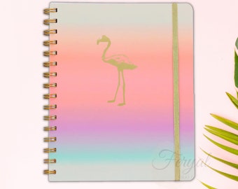 Op de afbeelding: Een spiraalgebonden notitieboek met een gradiëntomslag van lichtgroen naar roze en paars. Een gouden flamingo silhouet staat in het midden van de omslag. Een gouden elastiek en de spiraalbinding houden het notitieboek bij elkaar.
