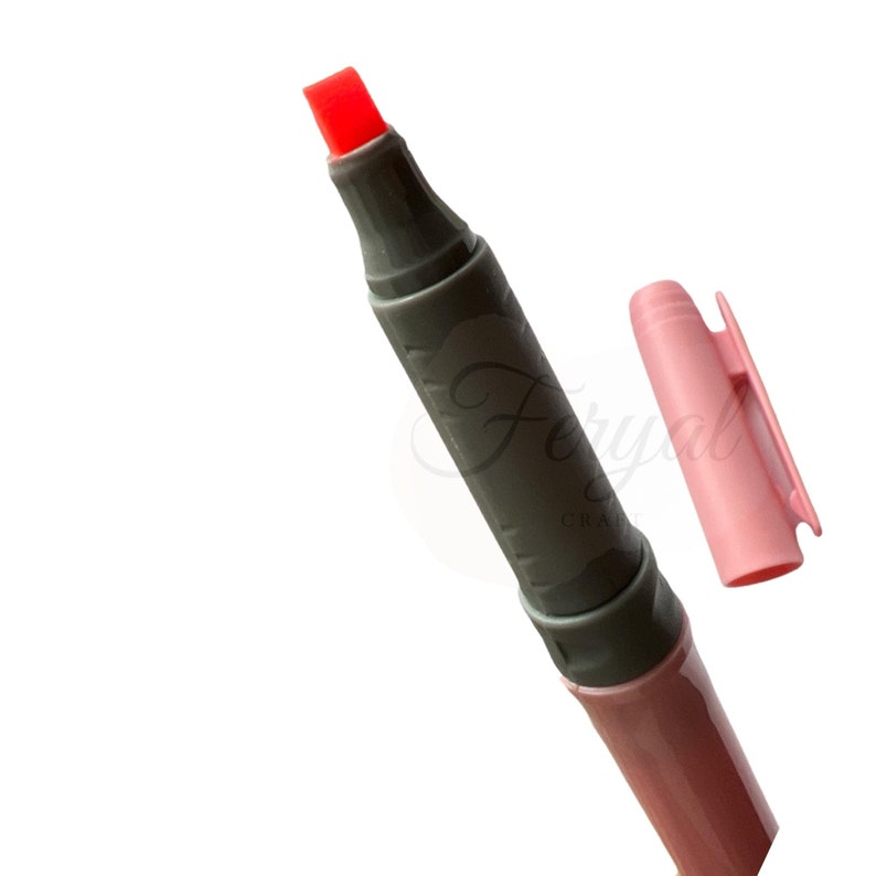 K&ouml;nnte beinhalten: Nahaufnahme eines rotspitzigen Markers mit grauem Schaft und rosa Kappe. Die Kappe ist abgenommen und neben dem Marker platziert. Der Marker tr&auml;gt den Text "Feryal Craft" auf dem Schaft.