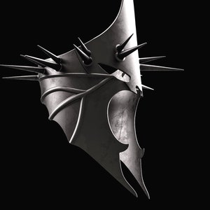 May include: A silver metal mask with a sharp, pointed design. The mask has a jagged, angular shape with spikes protruding from the top and sides.