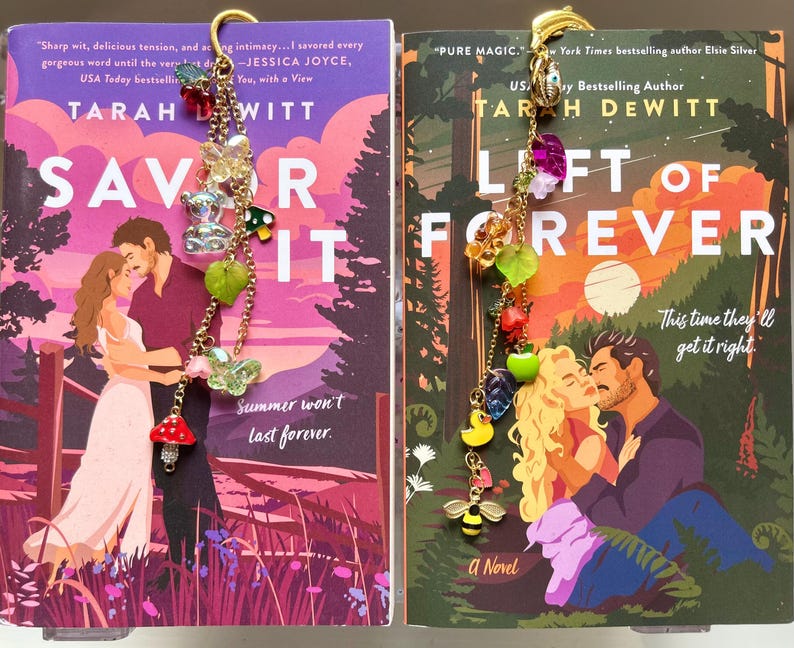 May include: Two books with colorful covers, titled "Savor It" and "Left of Forever," feature romantic illustrations. Decorative gold bookmarks with charms, including bears, butterflies, and fruit, are attached to the books. The books are novels.