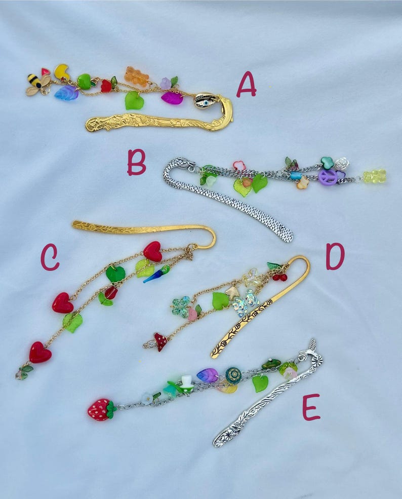 May include: A collection of decorative metal bookmarks with dangling charms. The bookmarks feature various designs, including gold and silver finishes, and are adorned with colorful beads, fruit, and whimsical shapes. Each bookmark has a unique charm arrangement.