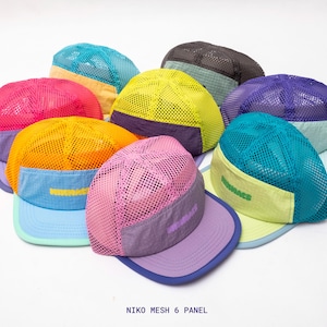 Puede incluir: Una colección de gorras de seis paneles con coronas de malla y viseras de tela sólida en varias combinaciones de colores, incluyendo amarillo neón, rosa, naranja, morado y turquesa. Cada gorra muestra el texto NIKO MESH 6 PANEL en el frente.