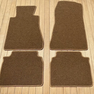 以下が含まれることがあります： 薄い茶色の縁取りが付いた、茶色の車のフロアマット4枚セット。マットは質感のある生地で作られています。